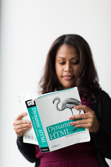 A woman with medium-length dark hair and medium skin tone is holding an open book titled 'Dynamic HTML,' displaying a detailed black-and-white illustration of a flamingo on the page. She is dressed in
